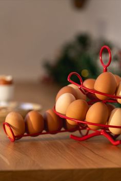 several eggs are stacked on top of each other in a red wire basket and placed on a wooden table