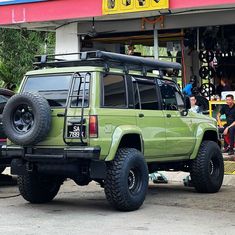 a green jeep is parked in front of a gas station with people standing around it