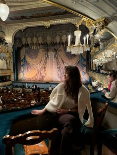 two women sitting at a table in front of a stage with chandeliers hanging from the ceiling