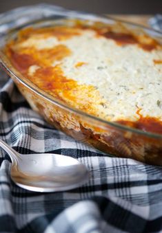 a casserole dish is sitting on a checkered table cloth with a spoon