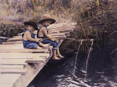 two young boys sitting on a wooden dock next to a body of water with reeds in the background