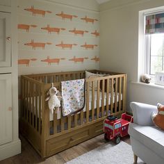 a baby's room with a crib, chair and wallpaper that has foxes on it