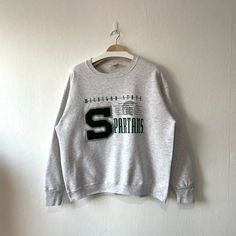 Vintage 90s Michigan State University Spartans Crewneck Sweatshirt (XL) Condition : Used vintage Good conditions Details : stains (Look at the picture) 📍Please Let me know if you have any questions or More Photo Detail Brand : Nutmeg Mills Made in : USA 🇺🇸 📍Measurement Size On Tag : XL Pit to pit : 24.5 inches Length : 25.5 inches 📍Material : Cotton Polyester Color : Light Gray ⛔️ Please keep in mind that our items are vintage so they may show some signs of wear and tear ⚠️ Please read ever Vintage College Sweatshirt, Thermal Hoodie, Michigan State University, Gray Sweatshirt, Embroidered Crewneck, Michigan State, How To Make Shorts, Tour T Shirts, Grey Sweatshirt