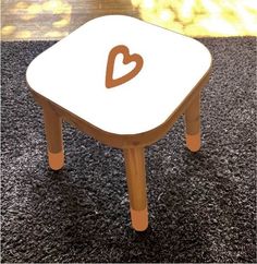 a small wooden table with a heart painted on it's side, sitting on carpet