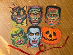 five halloween masks on a wooden surface with a red ribbon around them and one has an evil face, the other is a pumpkin