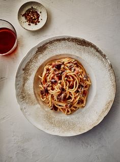 a white plate topped with pasta and sauce next to two bowls filled with red wine