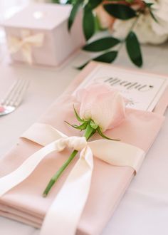 a pink napkin with a white rose on it next to a fork and spoons