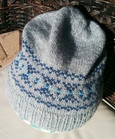 a blue and white knitted hat sitting on top of a wicker basket next to a brick wall