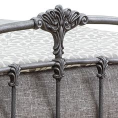 an ornate iron bed frame with white and gray patterned pillows on it's sides