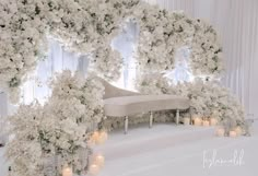 a white wedding setup with candles and flowers on the wall, along with a bench