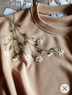 a sweater with white flowers on it sitting on top of a bed next to a pillow