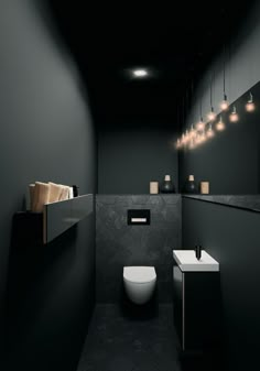 a black and white bathroom with lights hanging from the ceiling over the toilet, sink and mirror