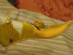 a yellow shoe with a flower on it sitting on top of a bed next to a pillow