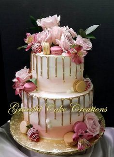 a three tiered cake decorated with pink flowers and chocolate candies on a gold platter