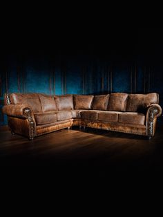 a brown leather sectional sofa sitting on top of a wooden floor next to a blue wall