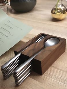 a wooden box with spoons and forks in it on a table next to a piece of paper