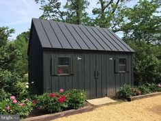 a small black shed sitting in the middle of some flowers