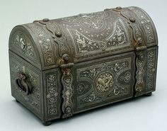 an old metal box with intricate designs on the lid and sides, sitting on a white surface