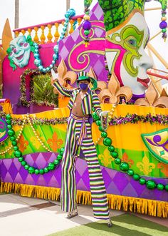 a woman in striped pants and clown makeup standing next to a carnival float with decorations on it