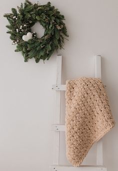 a crocheted blanket sitting on top of a ladder next to a wreath