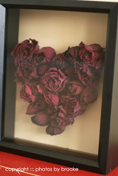 a heart made out of red roses in a shadow box with black frame on the wall