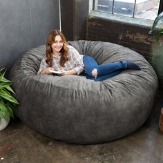 a woman laying on top of a large bean bag chair next to a potted plant