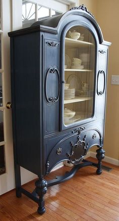 an old fashioned china cabinet is painted black and has glass doors on the front door