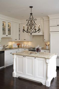 a white kitchen with an island and chandelier hanging from it's ceiling