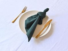 a white plate topped with green napkins next to gold utensils on top of a white table cloth