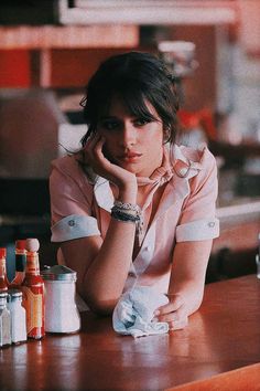 a woman sitting at a bar with her hand on her chin and other condiments behind her