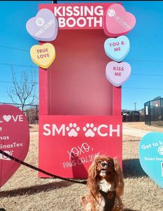 a dog sitting in front of a booth with hearts on it's sides and the words kissing booth above