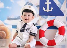 a baby boy in a sailor outfit sitting next to a life preserver