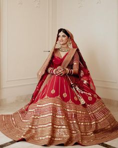 a woman in a red and gold bridal gown posing for the camera with her hands on her hips