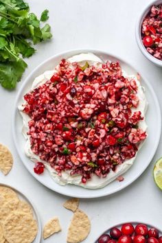 a white plate topped with fruit and crackers next to bowls of chips, lime wedges and cranberry salsa