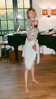 a woman standing in front of a piano drinking from a glass with her legs crossed