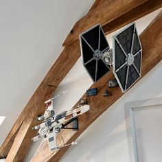 two star wars vehicles are hanging from the ceiling in a room with white walls and wood beams