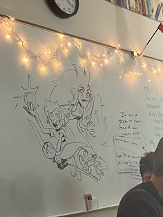 two people sitting at a table in front of a whiteboard with drawings on it