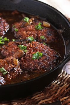 a skillet filled with meat covered in sauce and garnished with parsley