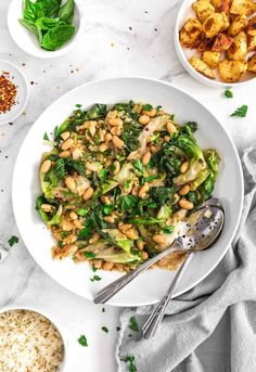 a white bowl filled with greens and chickpeas next to other bowls of food