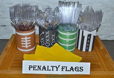 a wooden tray topped with plastic cups filled with candy and football themed paper napkins