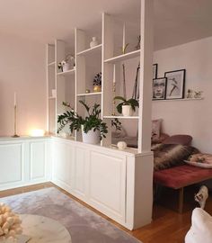 a living room filled with lots of white shelves and plants on top of it's bookshelves