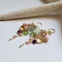 a pair of earrings with different colored stones and pearls hanging from it's earwires