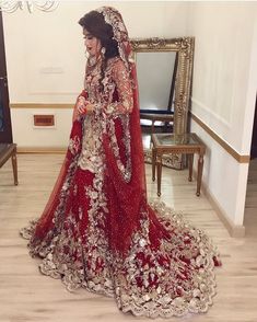 a woman in a red and gold bridal gown standing next to a mirror with her hands on her hips