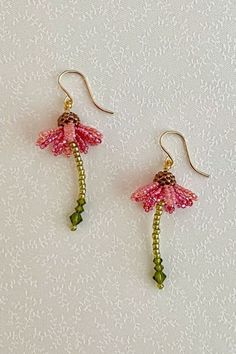 two pink flowers with green stems are hanging from gold earwires on a white background