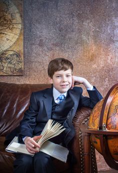 a young boy in a suit sitting on a couch with an open book and looking at the camera