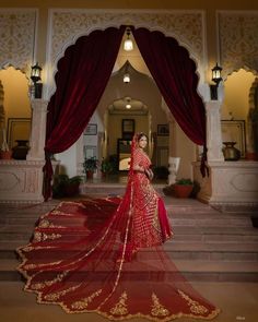 a woman in a red and gold bridal gown standing on some steps with her arms behind her back