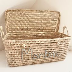 a woven basket with the word martin written in silver on it, sitting next to a white wall