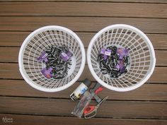 two white baskets filled with black and purple items on top of a wooden table next to scissors