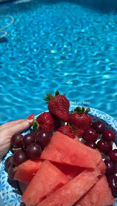 watermelon, grapes and strawberries on a plate next to a swimming pool