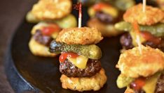 mini hamburgers with pickles and cheese on them are arranged on a black plate